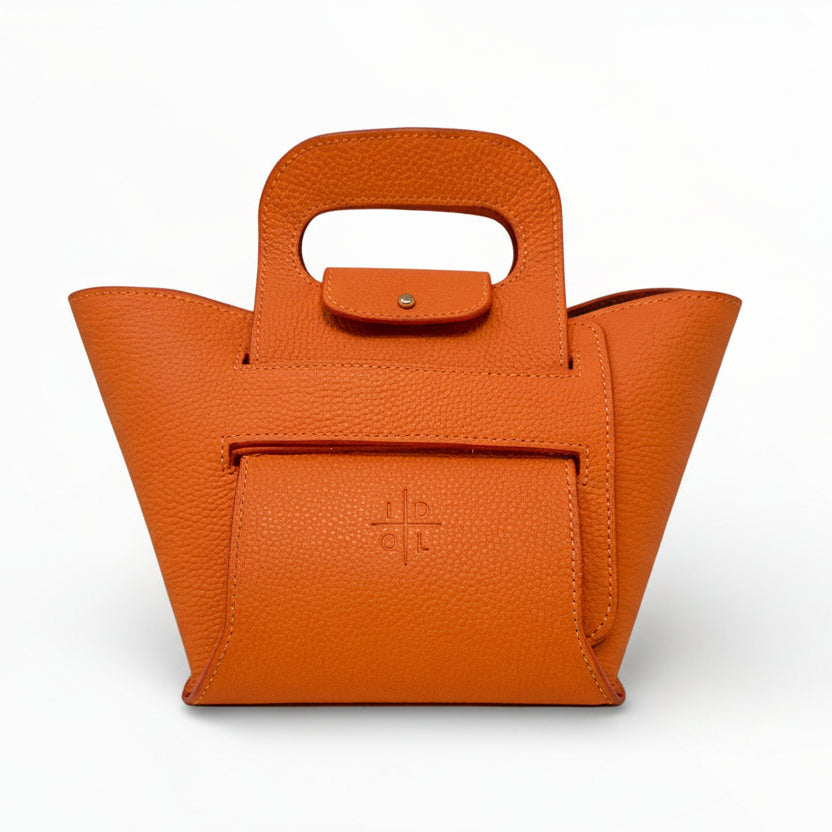 Front view of a orange collapsible handbag with pebbled finish, cutout handle, and embossed logo stamp.”