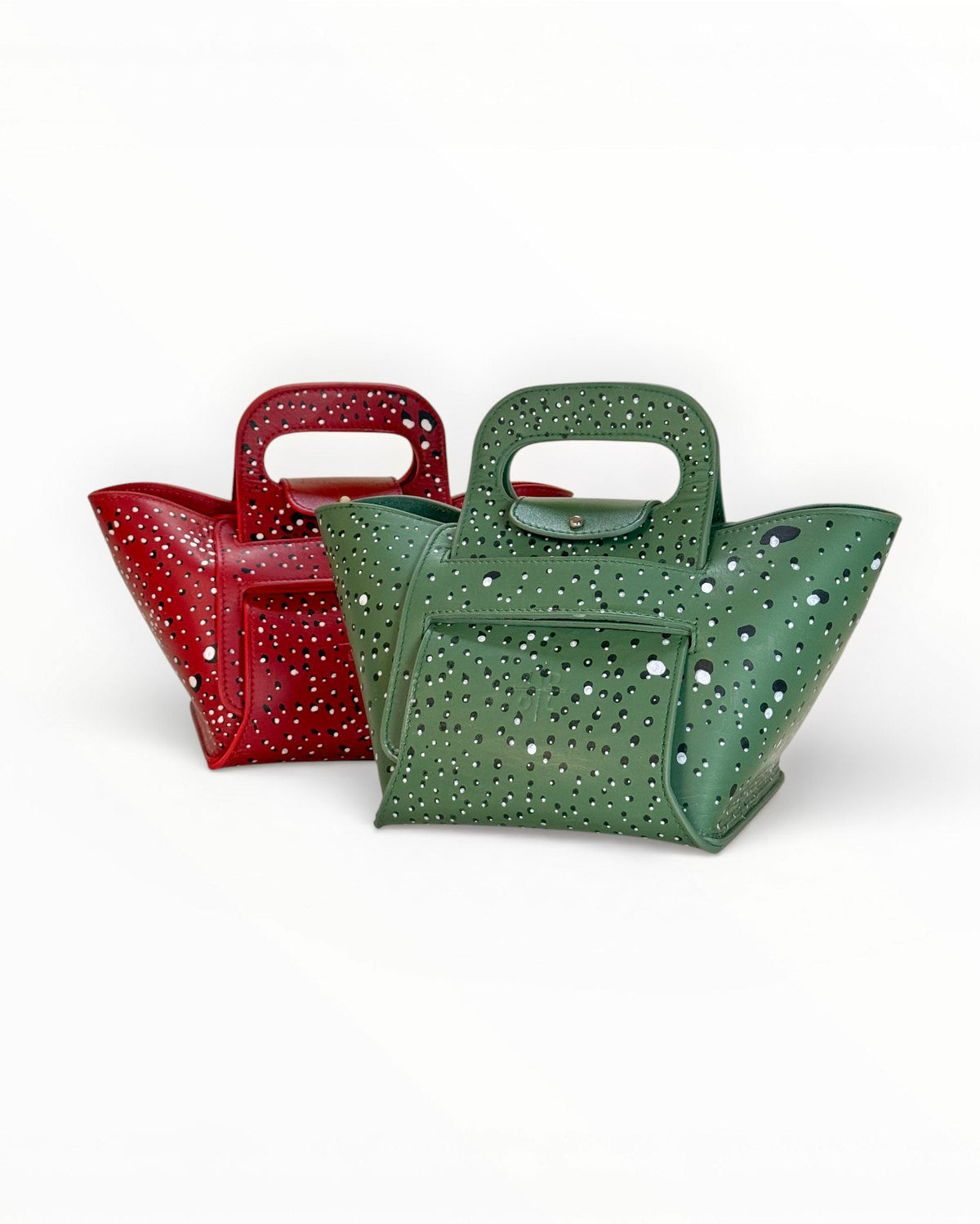 Two structured leather Zoe handbags with hand painted dot design and top handles, shown on a clean white background. One bag is red and one is green, both decorated with small black and white dots