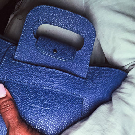 Close-up of a blue textured handbag held by a person with a blurred background