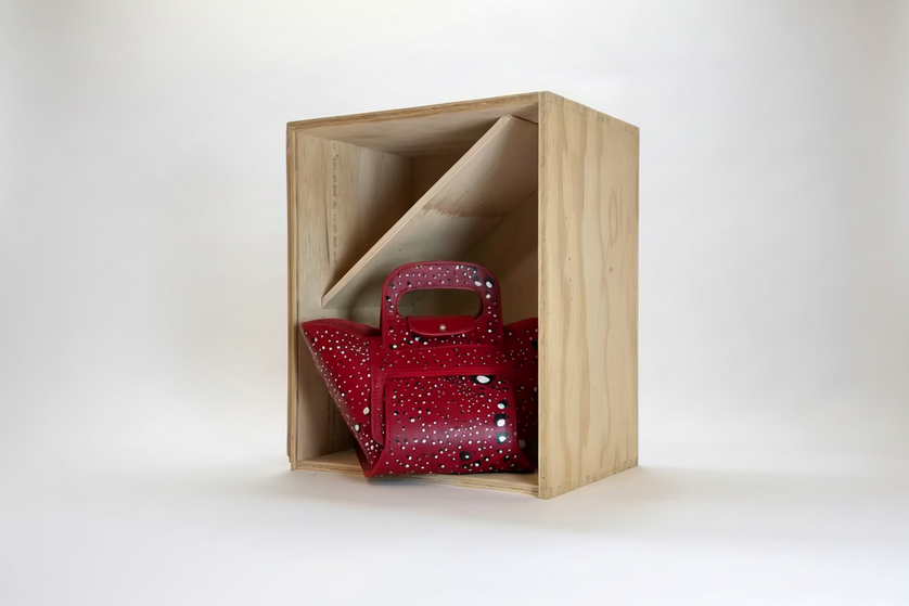Red handbag with hand paint details in a wooden box on a white background