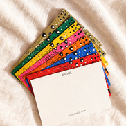 A fan of colorful, textured notepads with small black heart details on a beige linen fabric background. The top notepad is blank white with the text 'photo collection' printed on the side.