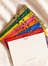 A fan of colorful, textured notepads with small black heart details on a beige linen fabric background. The top notepad is blank white with the text 'photo collection' printed on the side.