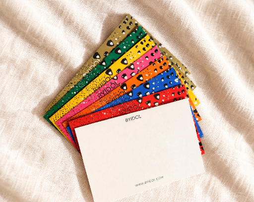 A fan of colorful, textured notepads with small black heart details on a beige linen fabric background. The top notepad is blank white with the text 'photo collection' printed on the side.